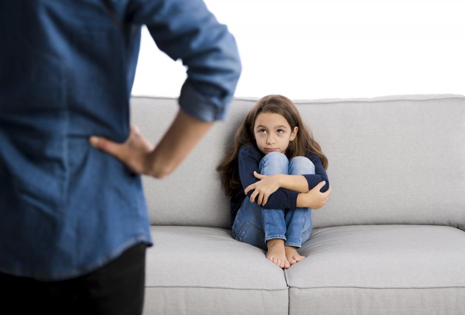 Junges Mädchen hat Angst vor Vater und kauert auf Sofa